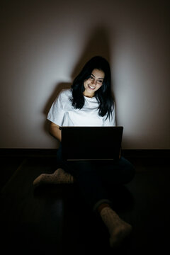 Young woman at home sitting on floor using laptop in the dark