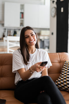 Happy young woman sitting on couch at home watching Tv