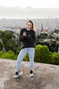 Young woman with camera above the city at sunrise, Barcelona, Spain