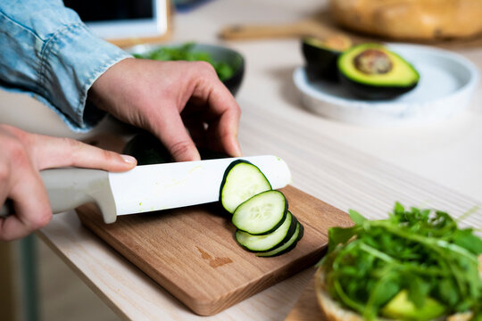Hands of woman slicing cucumber on cutting board