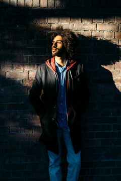 Portrait of a young man standing at a brick wall in shadow