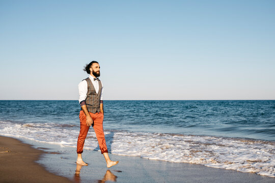 Well dressed man walking on a beach at water's edge