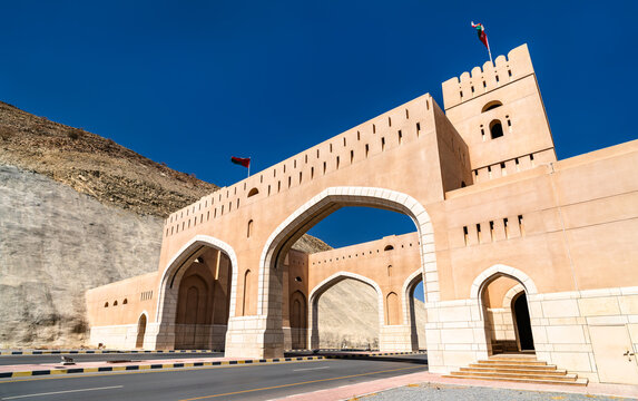 Architectural view of the monumental Rustaq City Gate, a traditional stone entrance structure located in the Al Batinah South Governorate of Oman under a clear blue sky.