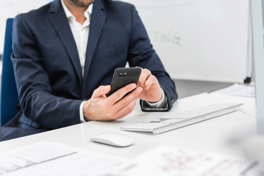 Close-up of businessman sitting at desk in office using cell phone