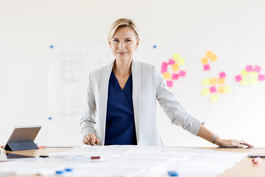 Portrait of confident blond businesswoman in conference room with adhesive notes at whiteboard