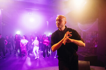 Male dance instructor demonstrates choreography in a vibrant dance studio with colorful lighting...