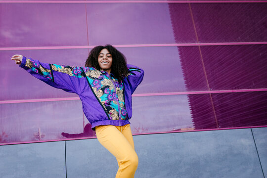 Young woman with urban look dancing, pink glass wall in the background