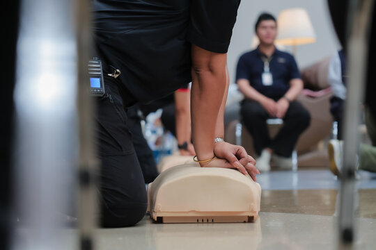 A close-up shows hands performing chest compressions on a CPR training dummy, demonstrating life-saving techniques during a first aid course.