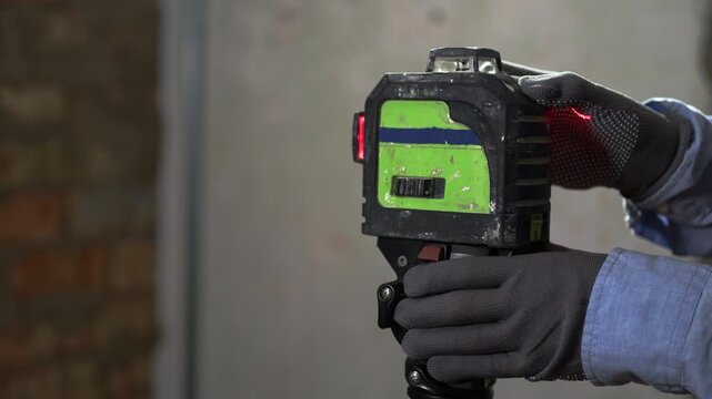 Builder in gloves is measures lines for laying tiles using a laser level with red beams.