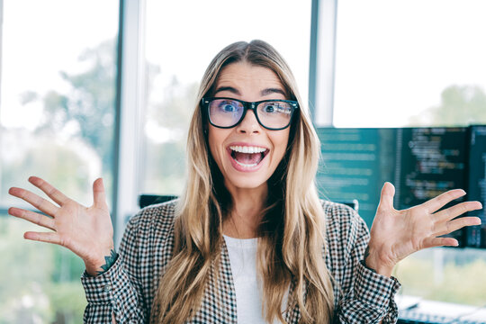 Excited female developer celebrating a coding success in a bright modern office wearing glasses and casual checkered shirt