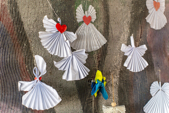 Irpin, Ukraine - 07 March 2026: View of handmade paper angels with red hearts and vibrant blue and yellow bird ornaments adorn a textured backdrop.