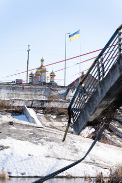Irpin, Ukraine - 07 March 2026: View of a broken bridge in the foreground leading to a church topped with golden domes under the crisp blue sky.