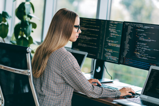 Female software developer coding at dual monitors in modern office workspace focusing on programming and web development
