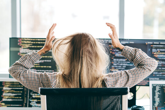 Frustrated software developer pulls at hair while debugging code on multiple monitors in bright modern office