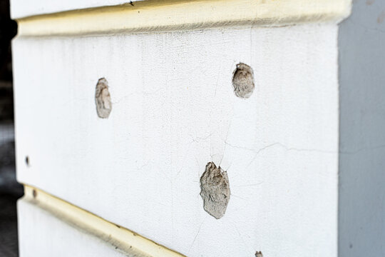 Irpin, Ukraine - 07 March 2026: View of a wall scarred with bullet holes, a stark reminder of conflict, its rough texture contrasting with the smooth, faded white paint.