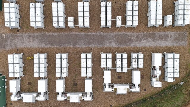 Aerial view of battery energy storage systems arranged in neat rows, contrasting sharply with the surrounding gravel and grass, Burwell, United Kingdom.