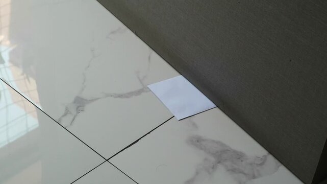 A white envelope with a message slipped under a door on a marble floor with natural light