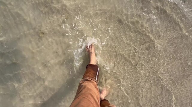 A man walks through shallow shoreline water in Sila, with soft waves and a calm Abu Dhabi&ndash;Saudi border coastline.