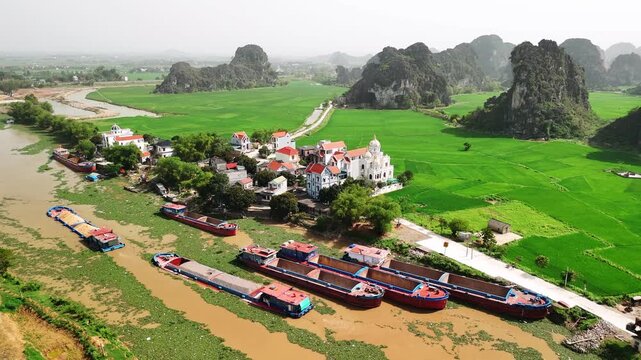 Aerial view of cargo barges floating on the river a rural village in ninh binh, vietnam with green rice paddies