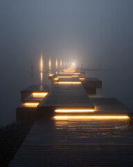 Fototapeta premium Foggy dock with illuminated boat and pier lights at dusk