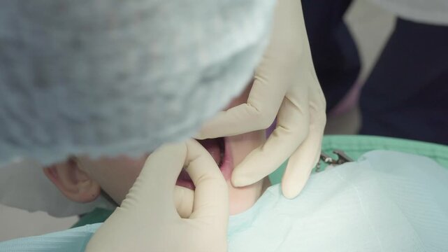 Dentist is fitting a chipped tooth in young boys mouth at dental office. He is working to put chipped tooth fragment back into place. Boy is sitting in dental chair