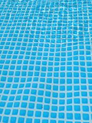 Clear water rippling over a blue swimming pool liner. Geometric square tile pattern distorted by...