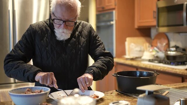 Elderly man shreds meat and cuts it in home kitchen while preparing carnitas with care and attention to the recipe.