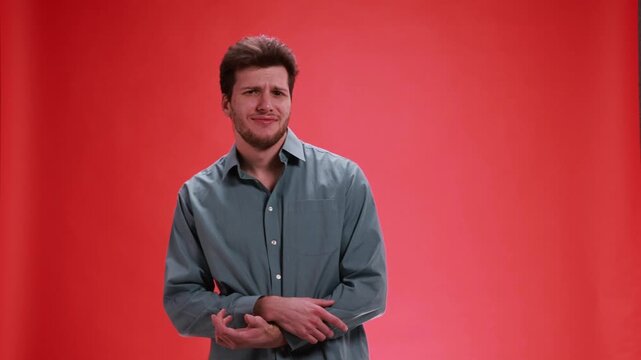 Young man reacting with confused doubtful expression on red studio background. Concept of misunderstanding situation, uncertainty reaction, questioning response, disbelief and awkward social moment.