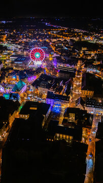 High angle drone view of the colorful Ferris wheel and the glowing streets of the Christmas market in Colmar, France, at night.