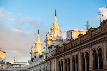 Fototapeta premium Twin ornate white spires with wrought iron finials rise over historic facades in Cordoba, Spain, as warm late day light reveals arcades and rooftop TV antennas.