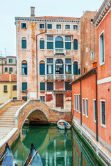 Fototapeta premium Venice canal in old town with historic buildings, small brick bridge and gondolas in traditional Italian cityscape. everyday transport and traditional architecture in the Venetian lagoon city, Italy