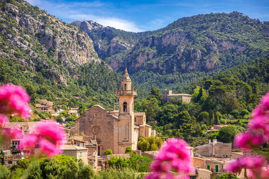 Scenic view of the Parish Church of Sant Bartomeu and historic stone houses in Valldemossa, Mallorca, nestled in the UNESCO World Heritage Serra de Tramuntana mountains in summer.