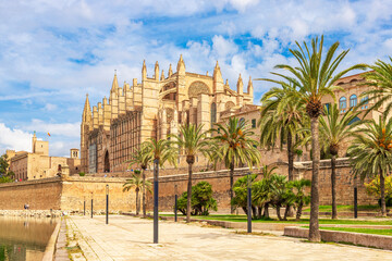 The Gothic Palma Cathedral (La Seu) and Royal Palace of La Almudaina framed by palm trees at Parc de la Mar in Palma de Mallorca, Spain.