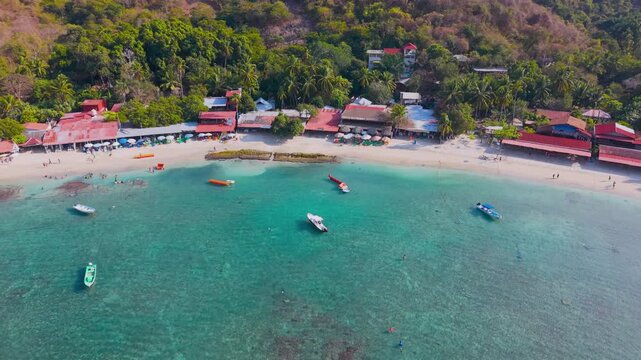 Aerial drone pan of Playa Las Gatas beach in Zihuatanejo Mexico revealing turquoise water boats restaurants and rocky reef coastline