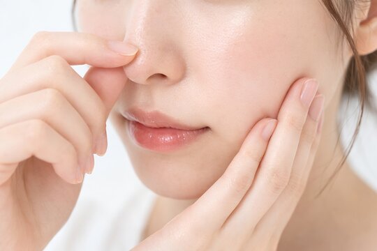 鼻の角栓やテカリなどの肌トラブルを気にして鏡を見ながら指で鼻を触るスキンケア中の女性