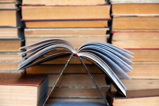 Open book placed upside down against wall of vintage books, literature and education concept, soft focus.