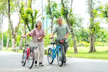 Obraz premium Asian senior woman and man leading the bicycles on the road together in the public park with day light and they look happiness.