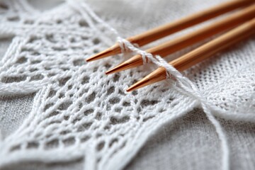 Knitting needles with white yarn and delicate lace fabric, close up of handmade textile craft and detailed knitting process on soft background.
