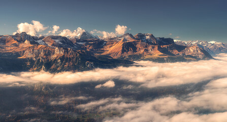 Panoramic aerial view of the Swiss Alps with snow-capped peaks and low clouds at sunset. Bright...