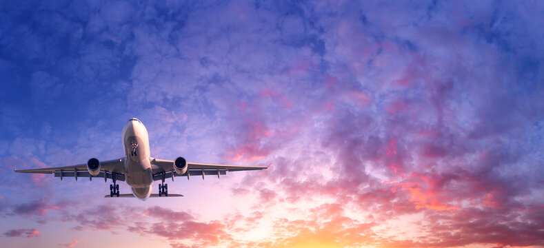 Commercial passenger airplane taking off. Aircraft flying up into dramatic pink and purple cloudy sky at sunrise. Air transportation and travel concept and background. Business trip