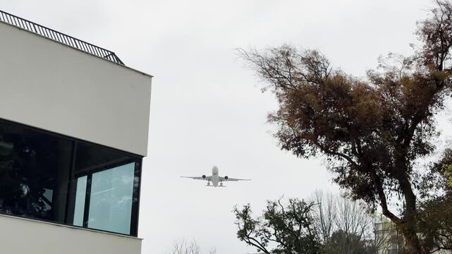 Airbus 330 comes in to land over the city at a very low altitude. A large white passenger plane flies low over the city. Silhouette of a flying airplane against the background of the sun at noon.