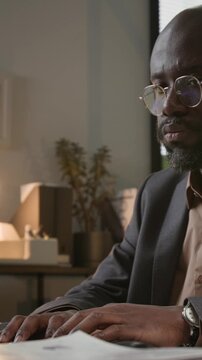 Vertical shot of African American man typing frantically at desk while keeping eye on hourglass and juggling heavy workload