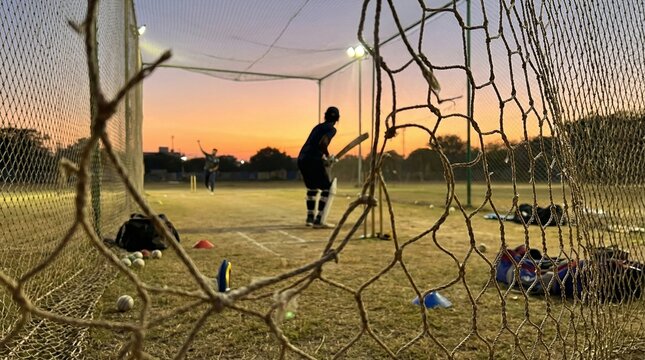 Cricketer practicing batting in nets during sunset at cricket field  