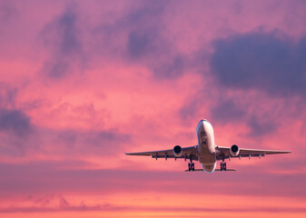 Commercial passenger airplane taking off. Aircraft flying up into dramatic pink and orange cloudy sky at sunrise. Air transportation and travel concept and background. Business trip