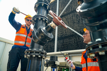 Two male technicians in safety vests and hard hats working on industrial cooling tower pipes