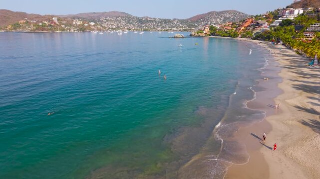 Aerial drone view of paddleboarders in turquoise water along Playa La Ropa beach in Zihuatanejo Mexico