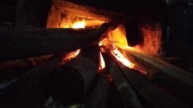 Close-up video of burning firewood inside a traditional wood stove with glowing flames and hot embers. The fire creates a warm and dramatic atmosphere, representing natural energy, cooking fire, rusti