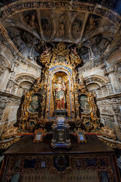 Baroque chapel interior with gilded retablo and Virgin and Child, Seville, Spain. Warm spot lighting heightens gold tones as silver candlesticks rest on the mensa.