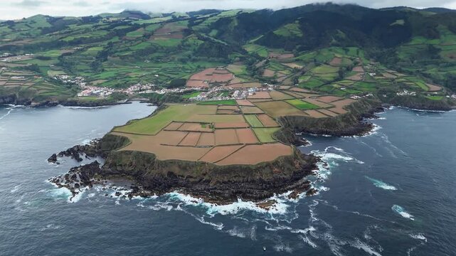 Patchwork terraced fields covering volcanic headland with steep basalt cliffs facing Atlantic Ocean, aerial view