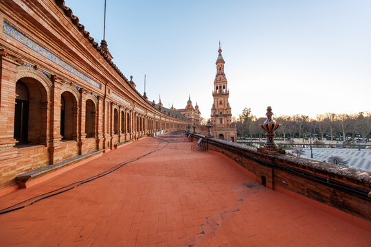 Seville, Spain. Plaza de Espana's arched colonnade and bell tower show terracotta brick, blue and white azulejo trim, and a curving terrace in soft late day light.